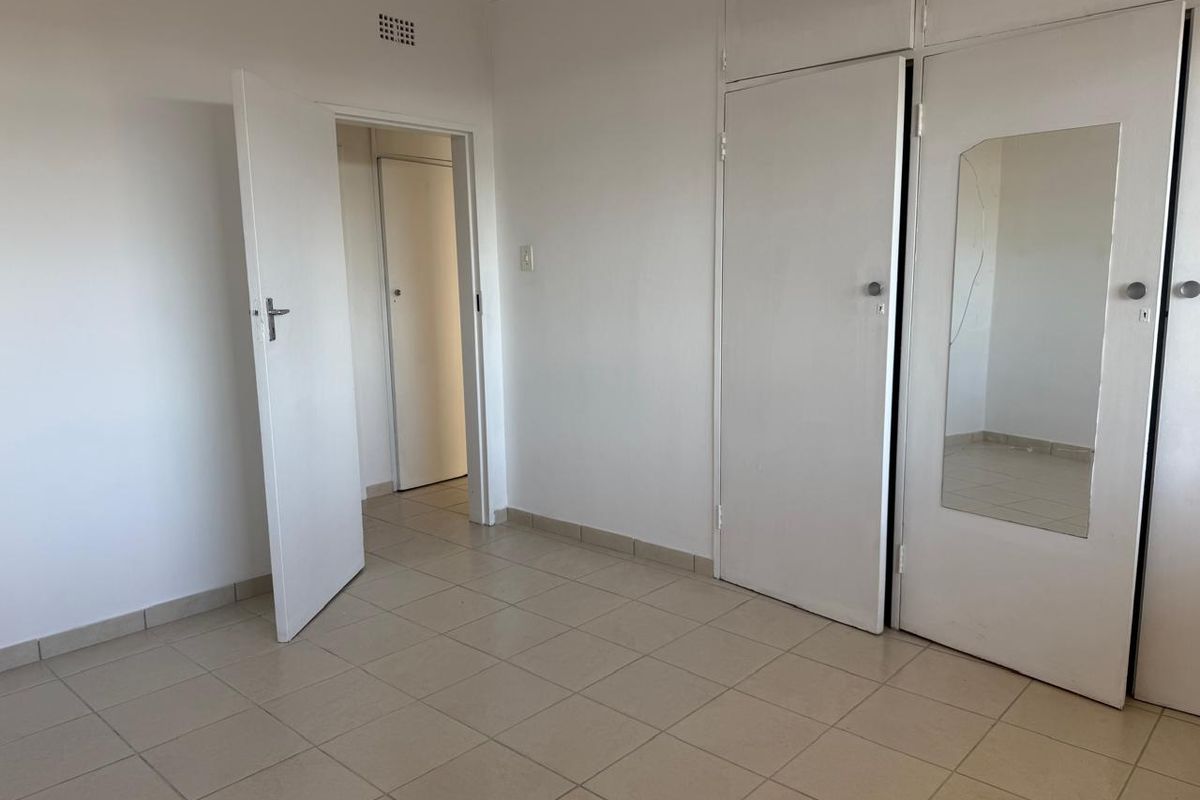 An empty bedroom featuring tiled flooring and built-in cupboards with a mirrored door panel.