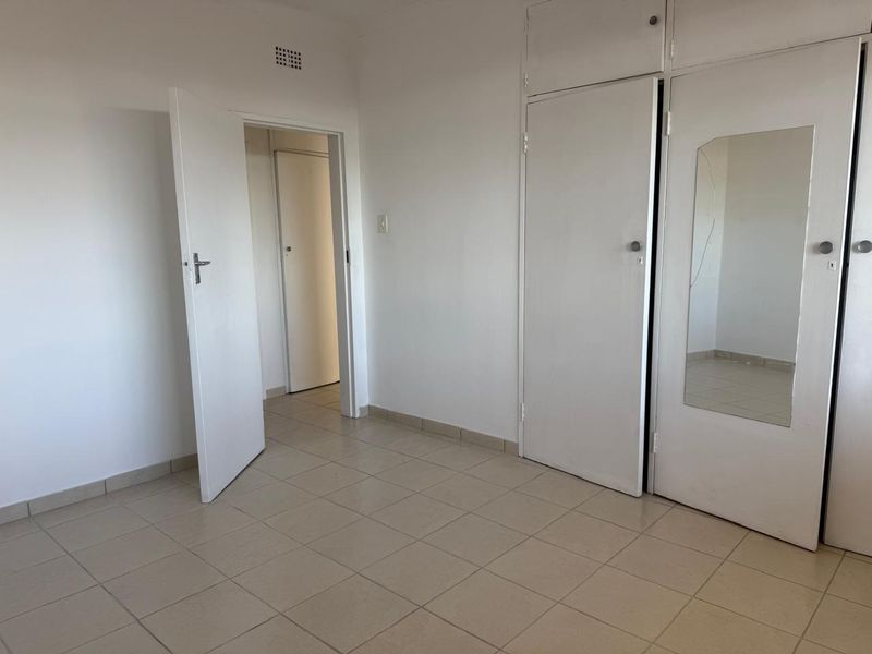 An empty bedroom featuring tiled flooring and built-in cupboards with a mirrored door panel.
