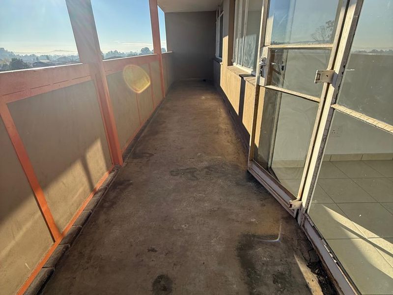 A long, open-air balcony featuring concrete flooring, metal balustrades, and glass sliding door access to the interior living space.