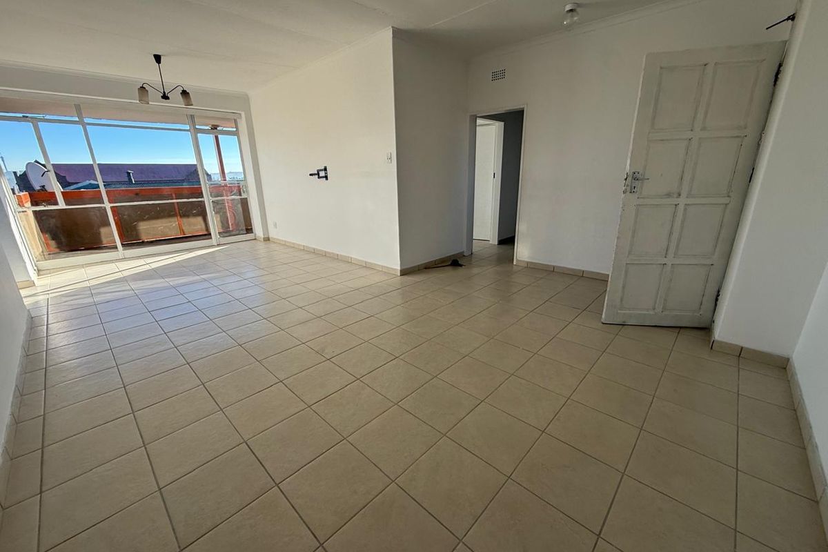 An empty, open-plan living area featuring neutral tiled flooring, a large sliding glass door providing natural light, and access to an adjoining balcony.