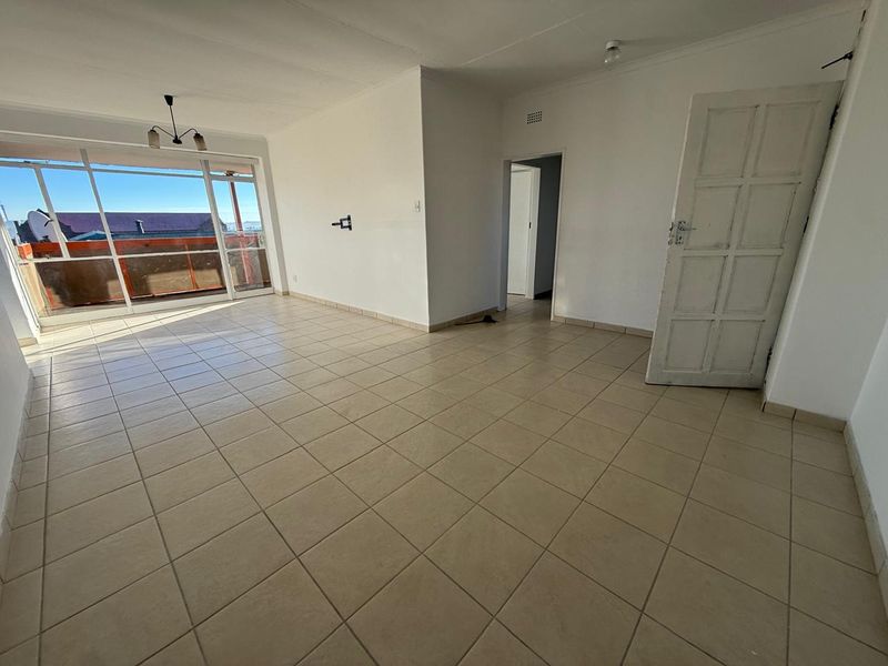 An empty, open-plan living area featuring neutral tiled flooring, a large sliding glass door providing natural light, and access to an adjoining balcony.