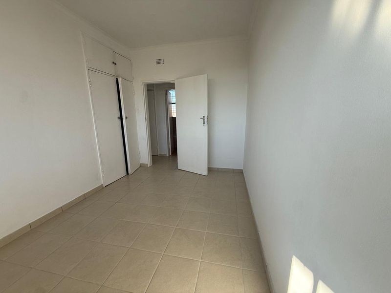 An empty bedroom featuring neutral tiled flooring and built-in cupboards, offering a clean, blank canvas ready for personalization.