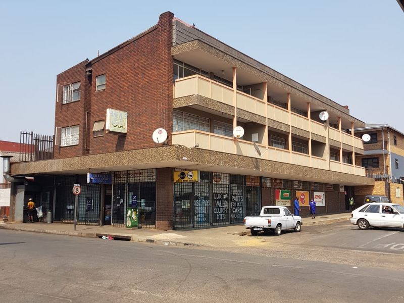 Street-level view of a multi-story brick apartment building featuring ground-floor commercial storefronts and upper-level residential balconies.