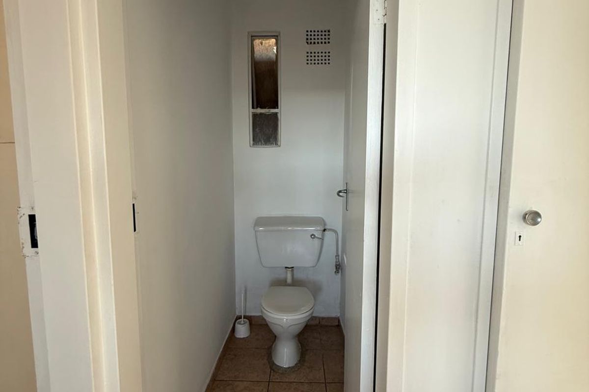 A compact, functional guest toilet featuring tiled flooring and basic sanitary fixtures, presenting an opportunity for modernization and cosmetic updates.