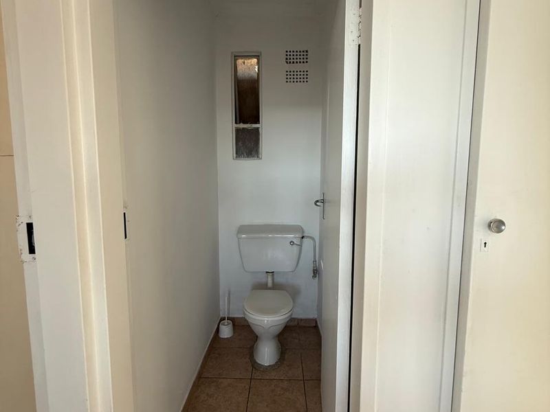 A compact, functional guest toilet featuring tiled flooring and basic sanitary fixtures, presenting an opportunity for modernization and cosmetic updates.