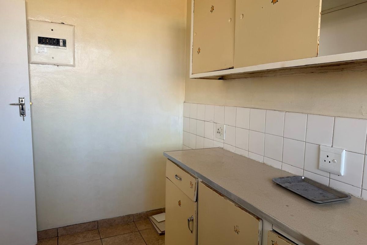 A dated kitchen area featuring original built-in cabinetry, tiled backsplash, and a laminate countertop, offering potential for a modern renovation.