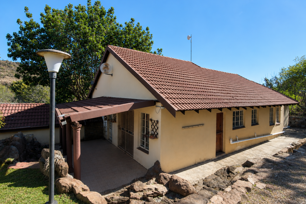 Rear view of the house featuring a covered patio, tiled roof, and established stone landscaping in a quiet setting.