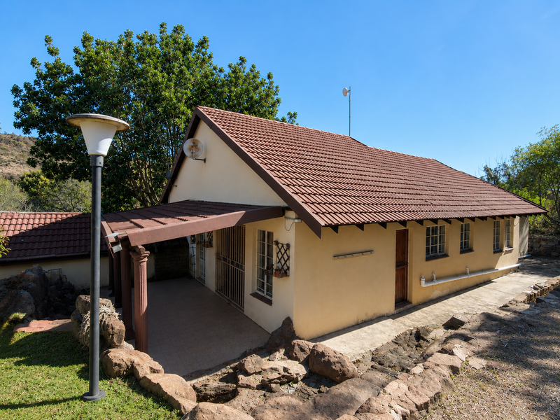 Rear view of the house featuring a covered patio, tiled roof, and established stone landscaping in a quiet setting.