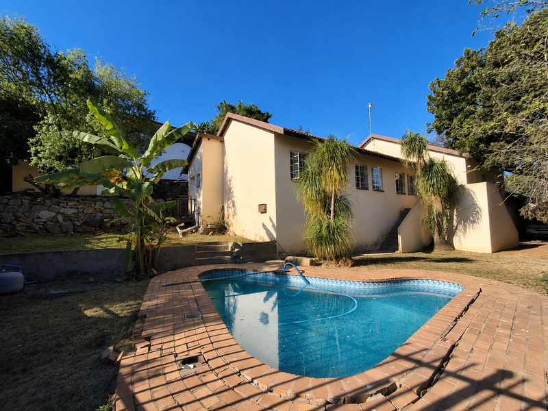Rear exterior view featuring a swimming pool with brick coping, stone retaining walls, and an external staircase leading to the upper level.