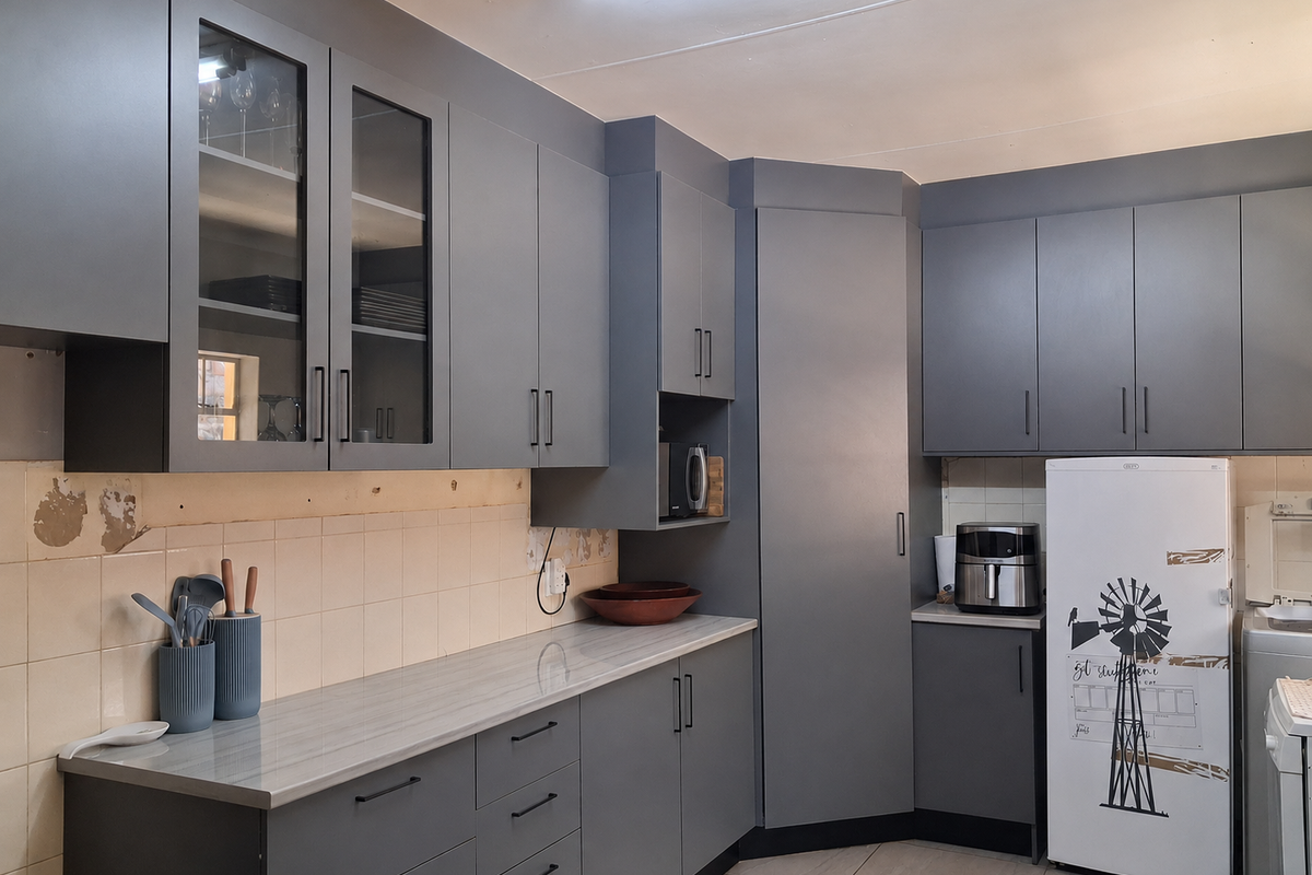 Modern grey kitchen featuring extensive cabinetry, laminate countertops, and a tiled backsplash, with some visible wall damage requiring repair.