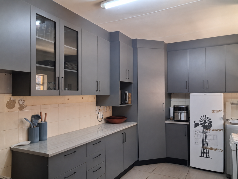 Modern grey kitchen featuring extensive cabinetry, laminate countertops, and a tiled backsplash, with some visible wall damage requiring repair.