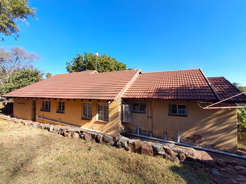 Rear view of the house featuring a tiled roof, stone retaining wall, and exterior walls showing signs of wear and plaster damage.