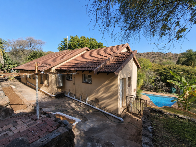 Rear view of the property featuring a tiled roof, concrete patio area, and an adjacent swimming pool set within a landscaped garden.