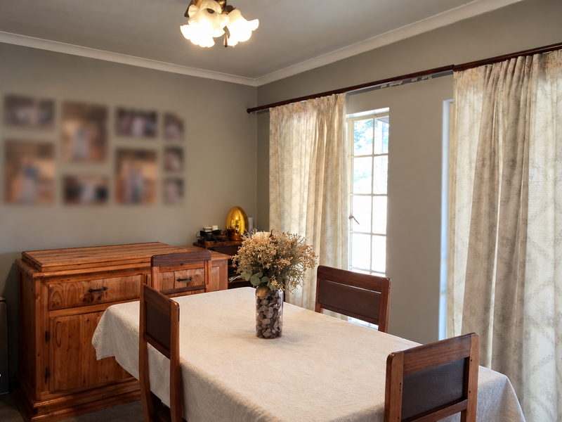 A dining room featuring neutral wall tones, a ceiling light fixture, and large windows with curtain treatments, providing a functional space for meals.