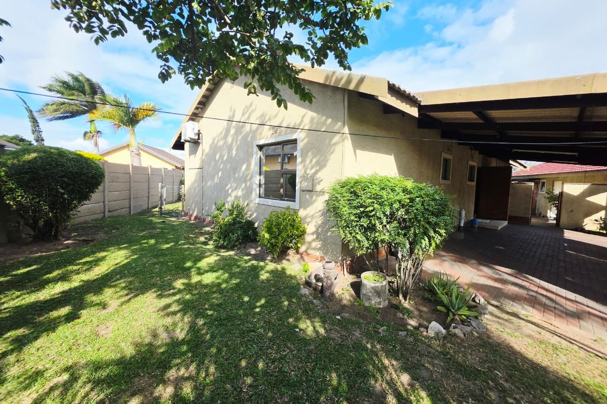 Rear exterior view of the property featuring a paved driveway, carport, and a private garden area with a precast boundary wall.