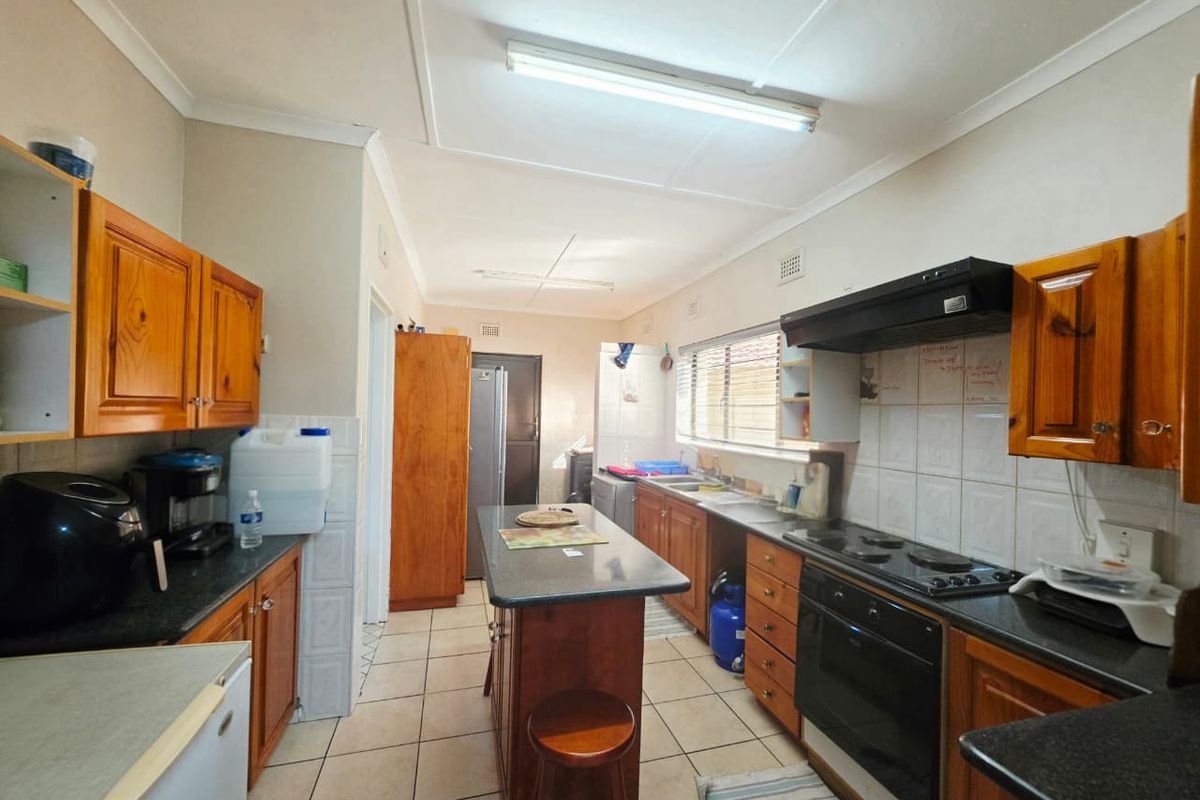 A functional kitchen featuring wooden cabinetry, a central island, built-in oven with extractor fan, and tiled flooring, offering a practical layout for daily use.
