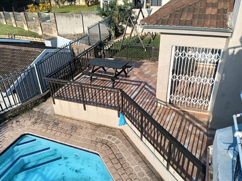Elevated patio area featuring tiled flooring and metal railings, overlooking the swimming pool and rear garden space.
