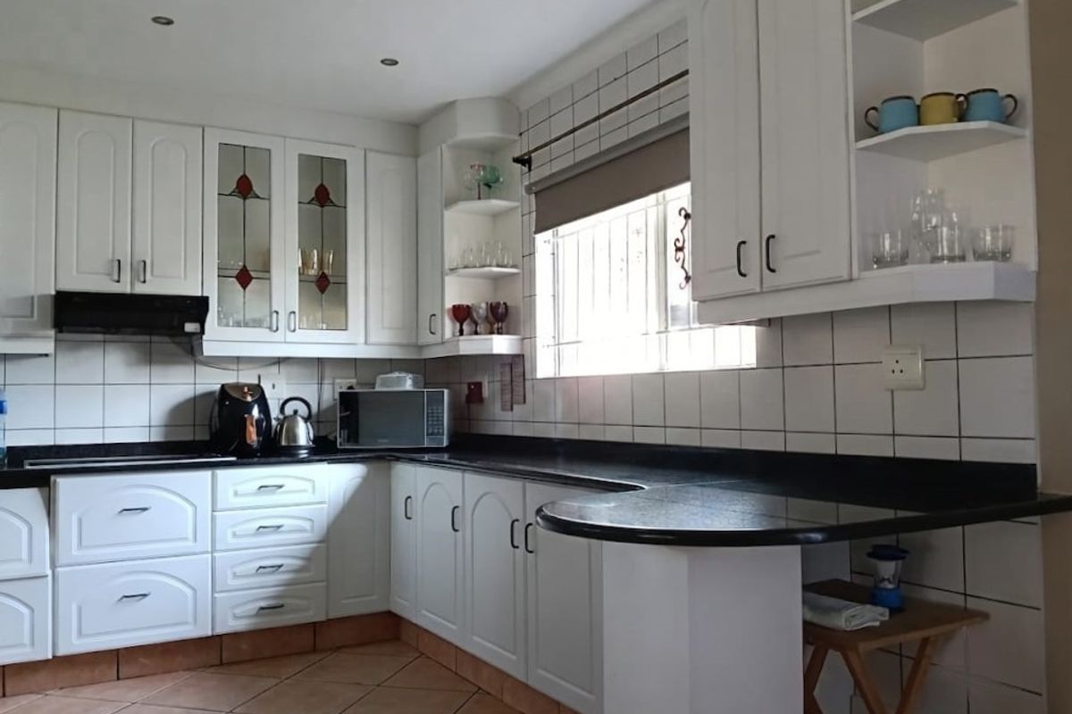 A functional kitchen featuring white cabinetry, black granite countertops, ceramic tile backsplash, and integrated storage shelving with a breakfast bar extension.