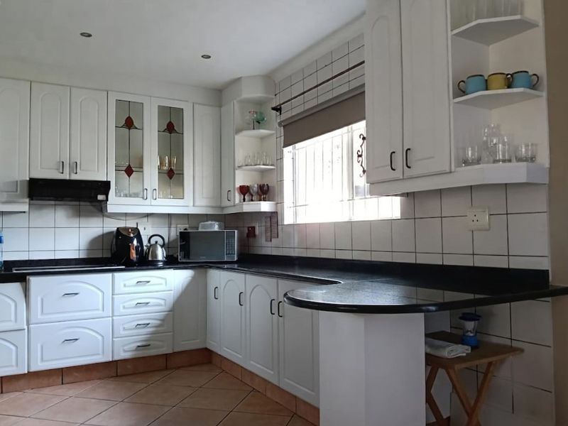 A functional kitchen featuring white cabinetry, black granite countertops, ceramic tile backsplash, and integrated storage shelving with a breakfast bar extension.