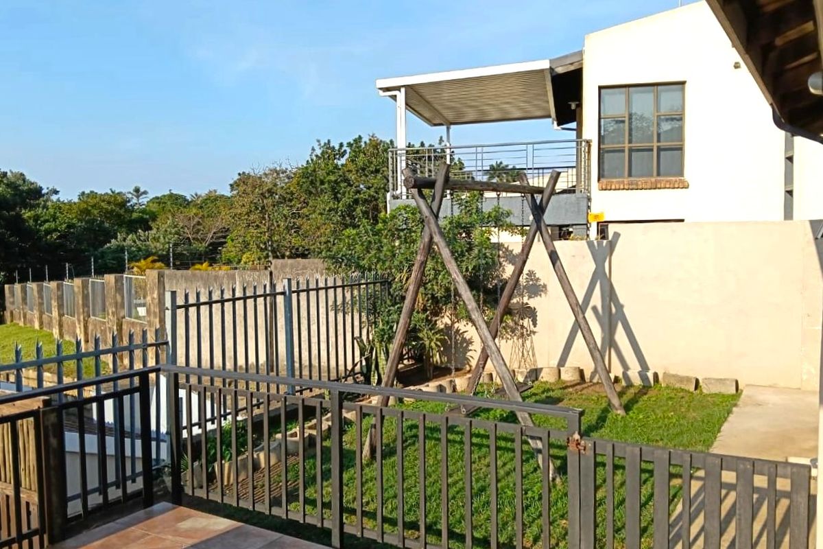 A view of the rear garden area featuring a tiled patio, metal fencing, and a covered balcony on the upper level of the house.