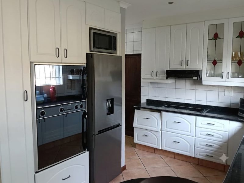 A functional kitchen featuring white cabinetry, granite countertops, tiled backsplash, and integrated appliances including an oven, microwave, and hob.