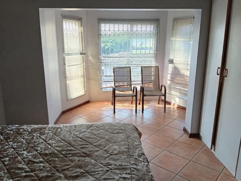 A bedroom featuring a bay window with security bars, tiled flooring, and built-in cupboards, offering a bright and functional living space.