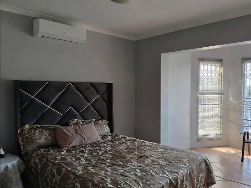 A well-maintained bedroom featuring tiled flooring, a wall-mounted split-system air conditioner, and large windows fitted with security bars.