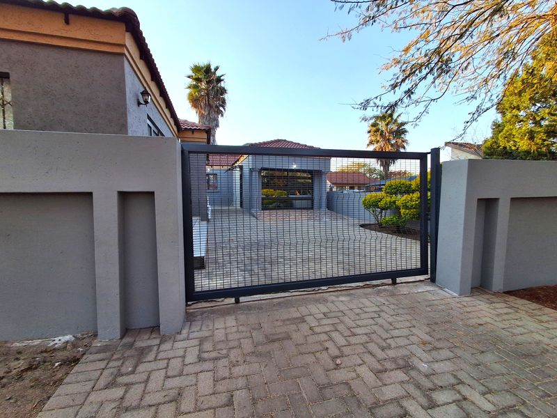 Front view of the property featuring a paved driveway, secure metal gate, perimeter wall, and a garage with a tiled roof.