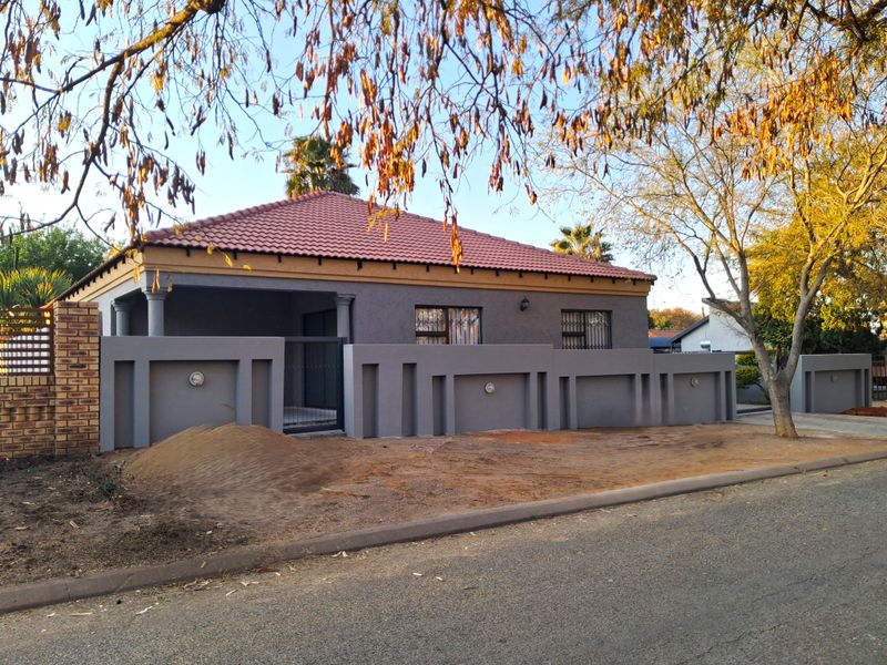 Front view of a single-story house featuring a tiled roof, covered porch, and a modern grey boundary wall with security gate.