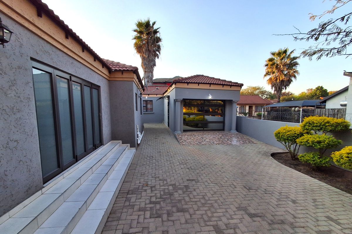 Rear exterior view featuring a paved driveway, tiled steps leading to sliding glass doors, and a detached garage structure.