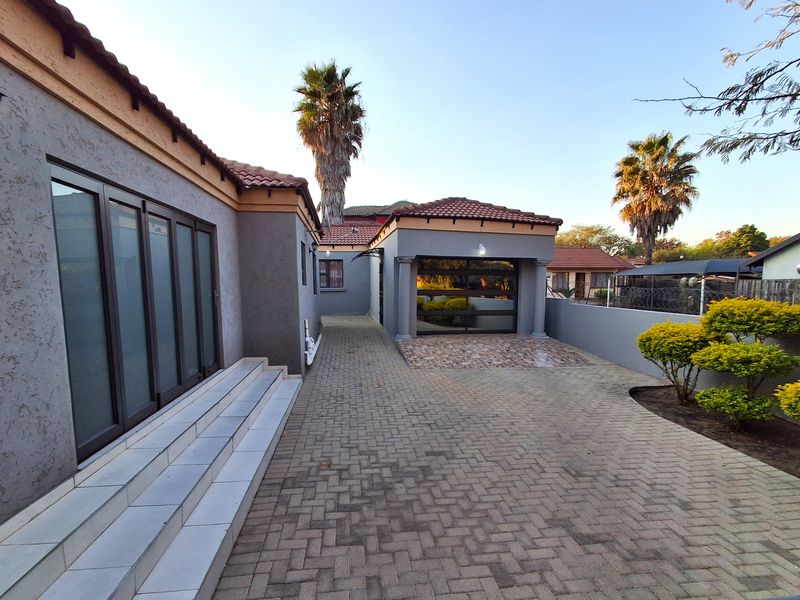 Rear exterior view featuring a paved driveway, tiled steps leading to sliding glass doors, and a detached garage structure.