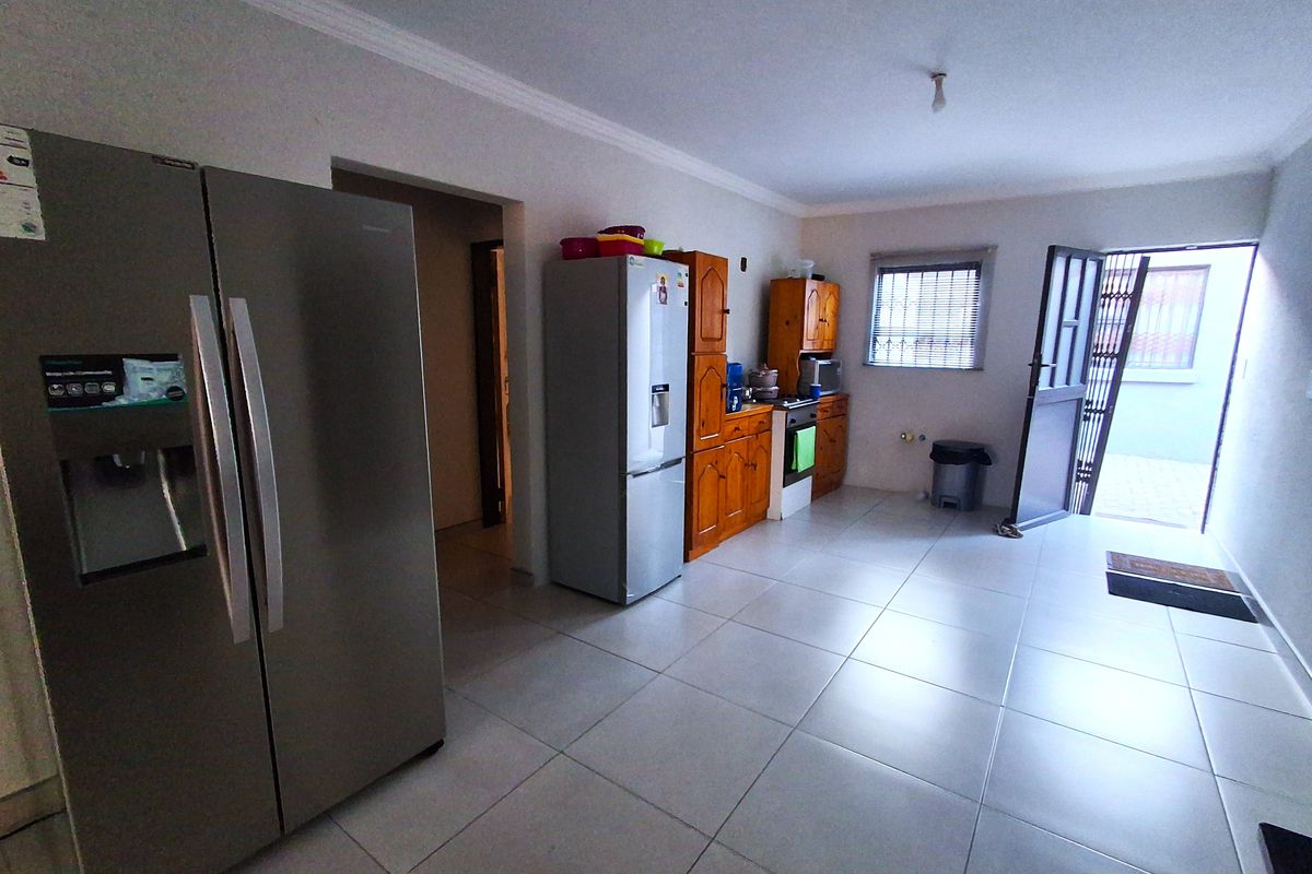 A functional kitchen featuring tiled flooring, built-in wooden cabinetry, and direct access to an outdoor area through a security gate.