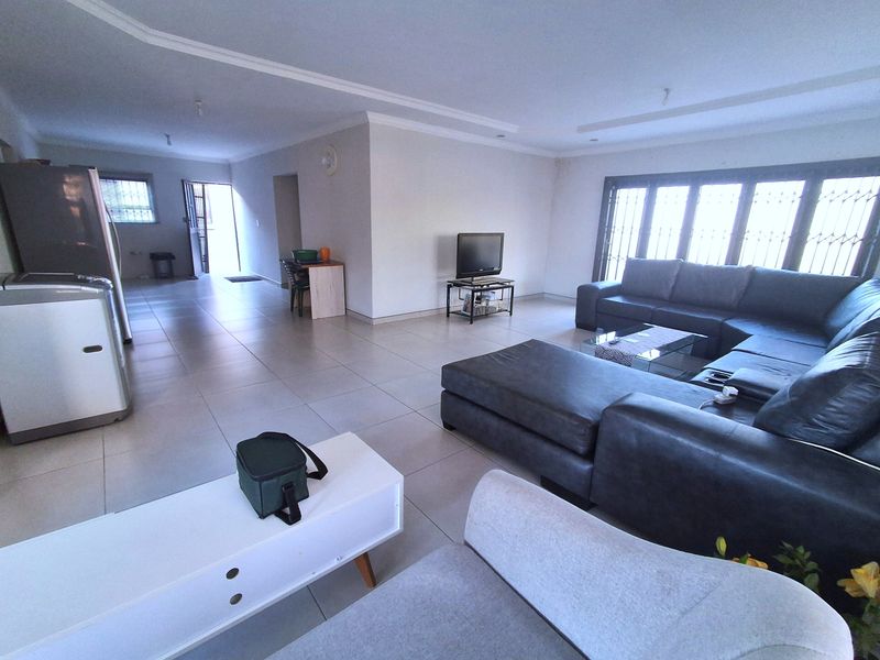 Spacious open-plan living area featuring neutral tiled flooring, recessed ceiling lighting, and large windows fitted with security bars.