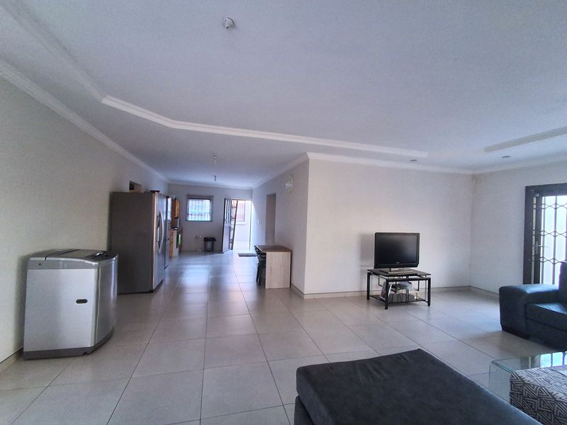 Spacious open-plan living area featuring neutral tiled flooring and recessed ceiling details, providing a versatile layout connecting to the kitchen and exterior access.