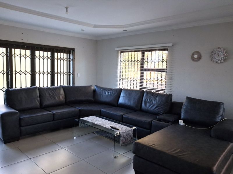 Spacious living room featuring neutral tiled flooring, a recessed ceiling design, and large windows fitted with security gates and venetian blinds.