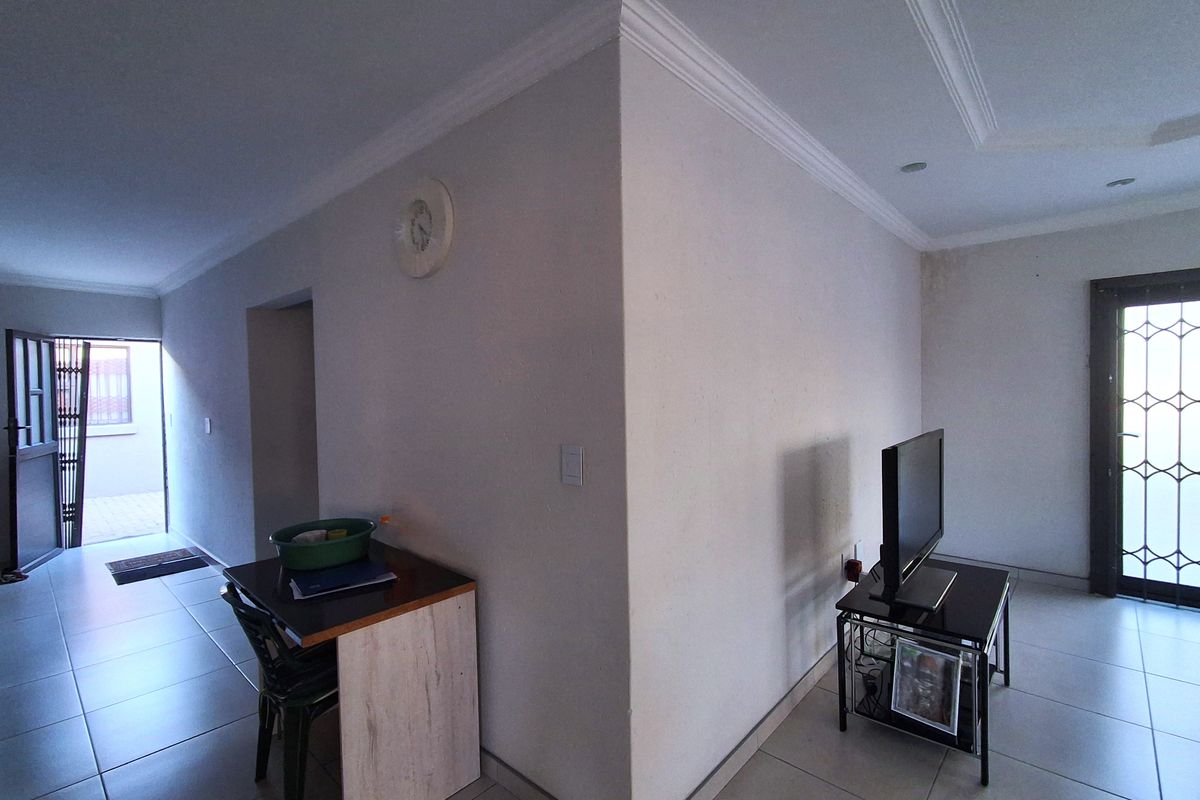 Living area featuring tiled flooring, decorative cornicing, and access to exterior spaces via security gates. Visible water staining on the wall requires attention.