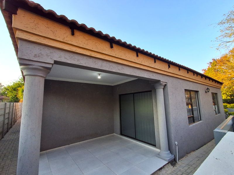 A covered patio area featuring tiled flooring, decorative concrete columns, and a sliding glass door providing access to the home interior.