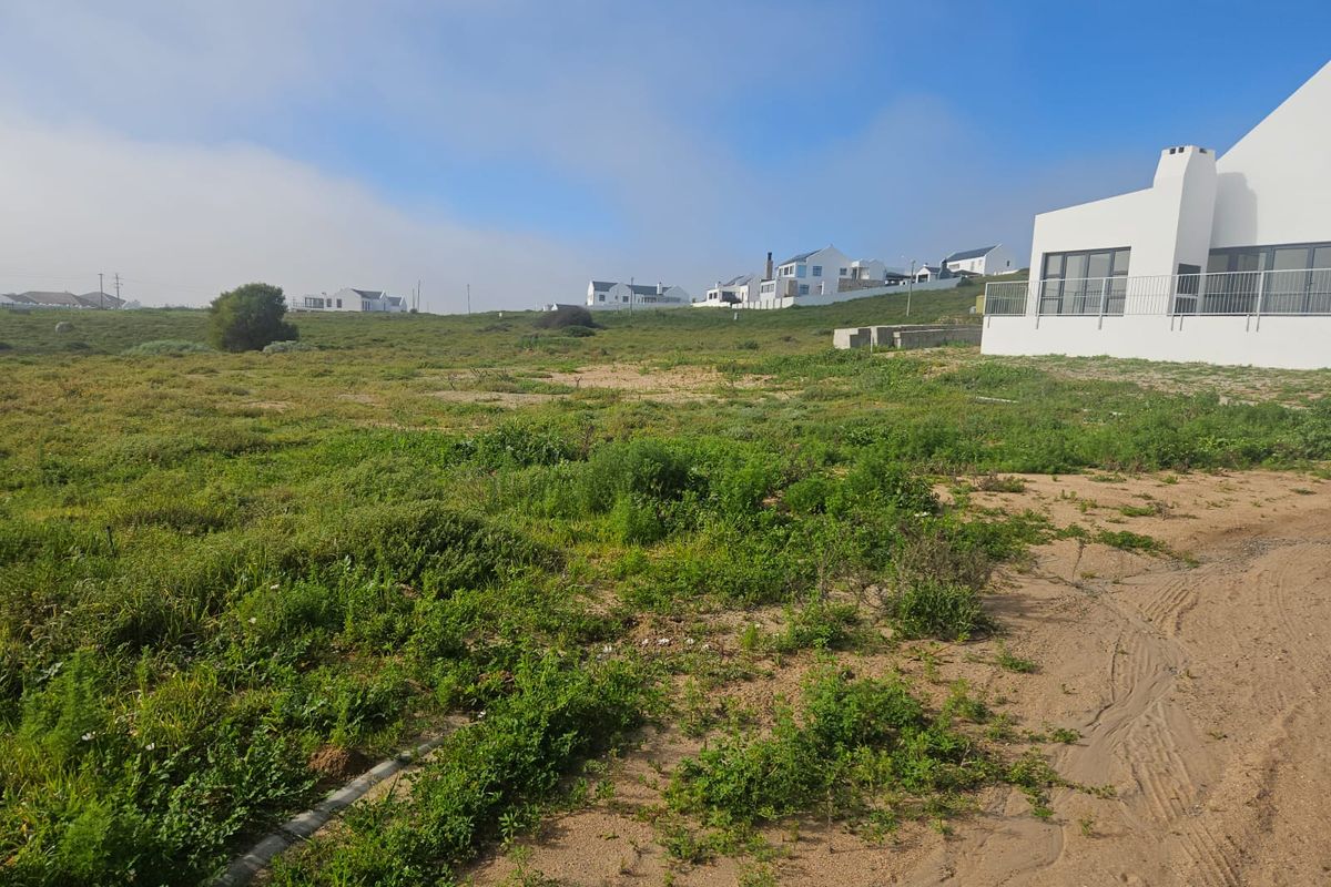 A view of a vacant residential plot featuring natural vegetation, with an adjacent modern white building visible in the background.
