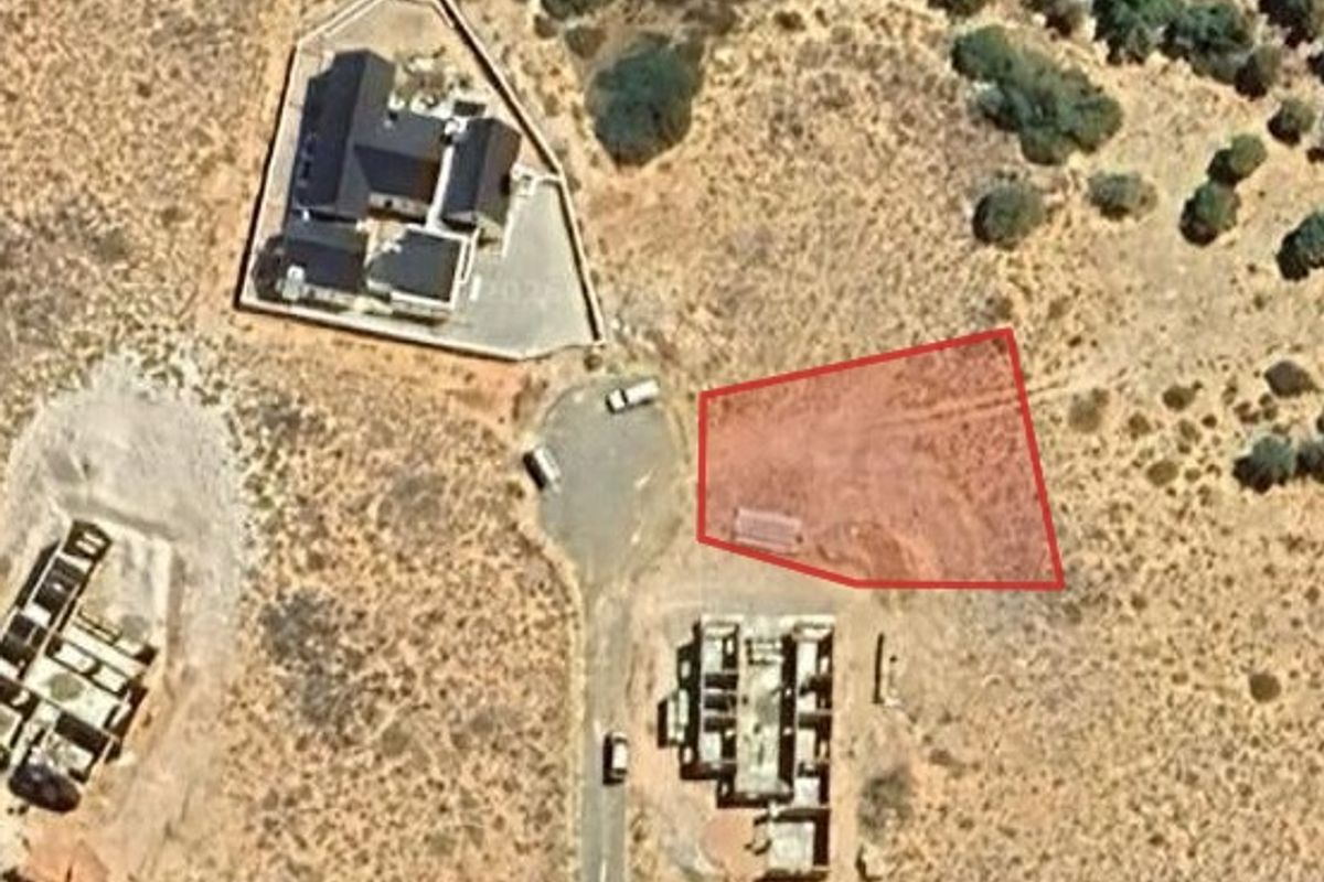 Aerial view of a vacant residential land plot highlighted in red, situated within a developing estate with established road access.