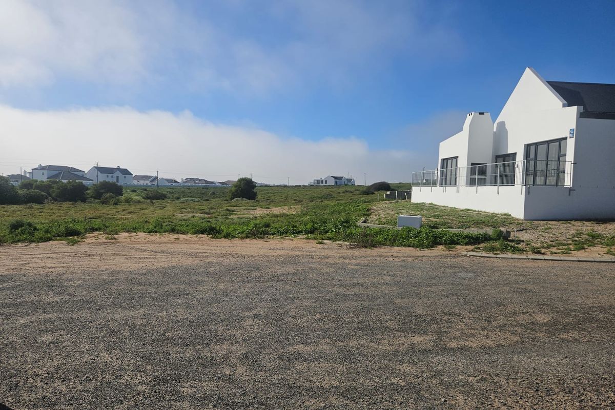 A view of the residential property exterior featuring a gravel driveway and a modern white building with a metal balustrade.