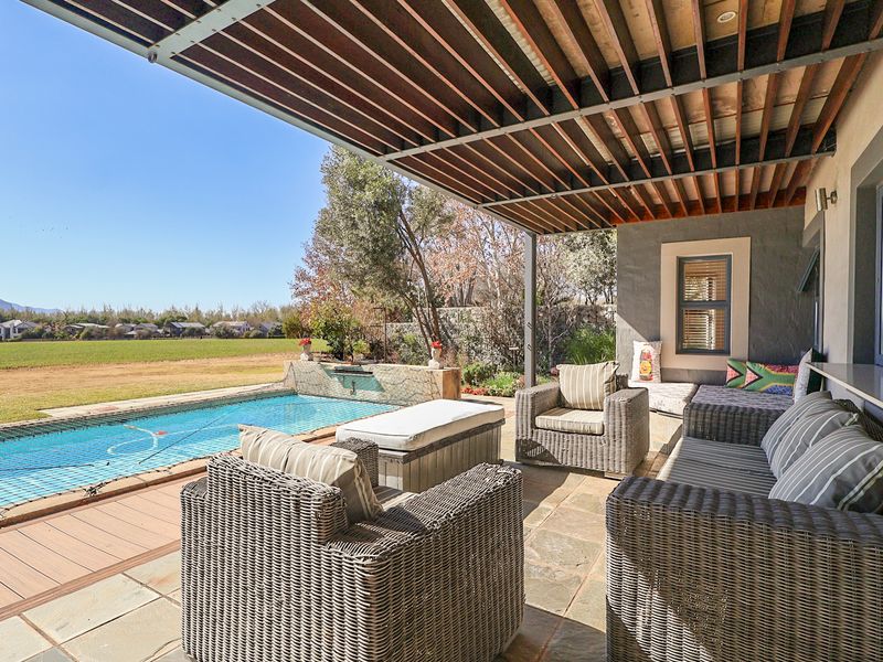 Covered patio area featuring stone flooring and a timber pergola, overlooking a private swimming pool with a water feature and scenic landscape views.