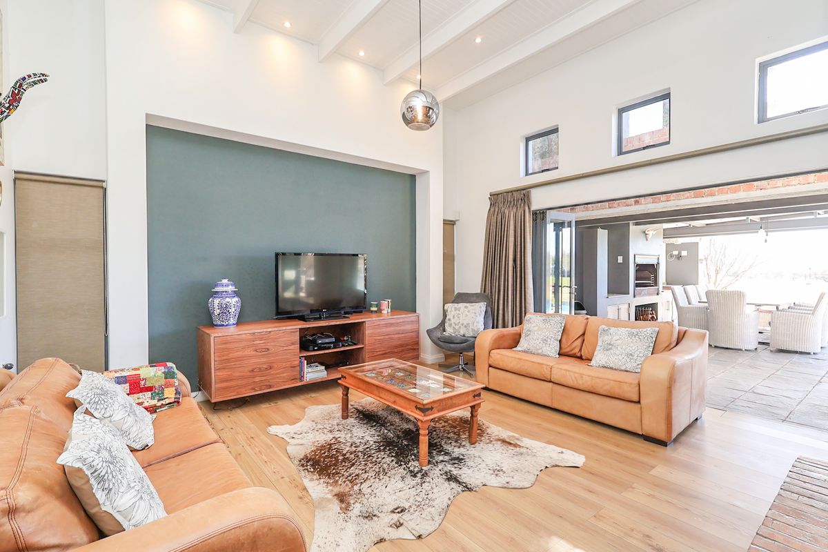 Spacious living room featuring high vaulted ceilings with exposed beams, hardwood flooring, and large sliding doors opening to an outdoor patio area.