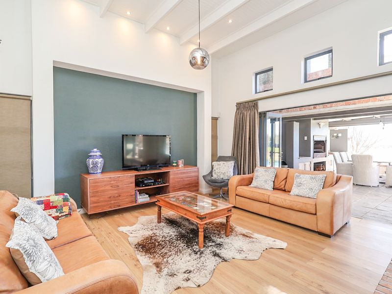 Spacious living room featuring high vaulted ceilings with exposed beams, hardwood flooring, and large sliding doors opening to an outdoor patio area.