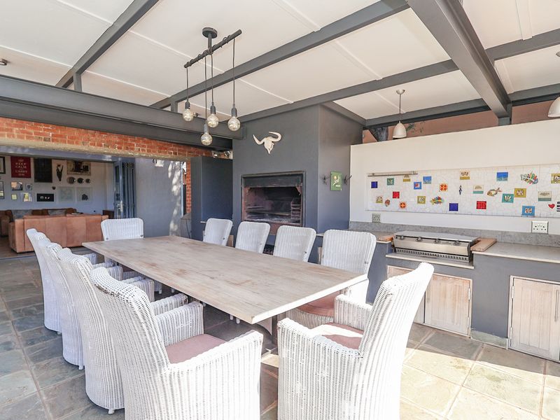 Covered outdoor patio featuring a built-in braai, integrated gas grill, stone flooring, and exposed steel beam ceiling, perfect for alfresco dining and entertaining.