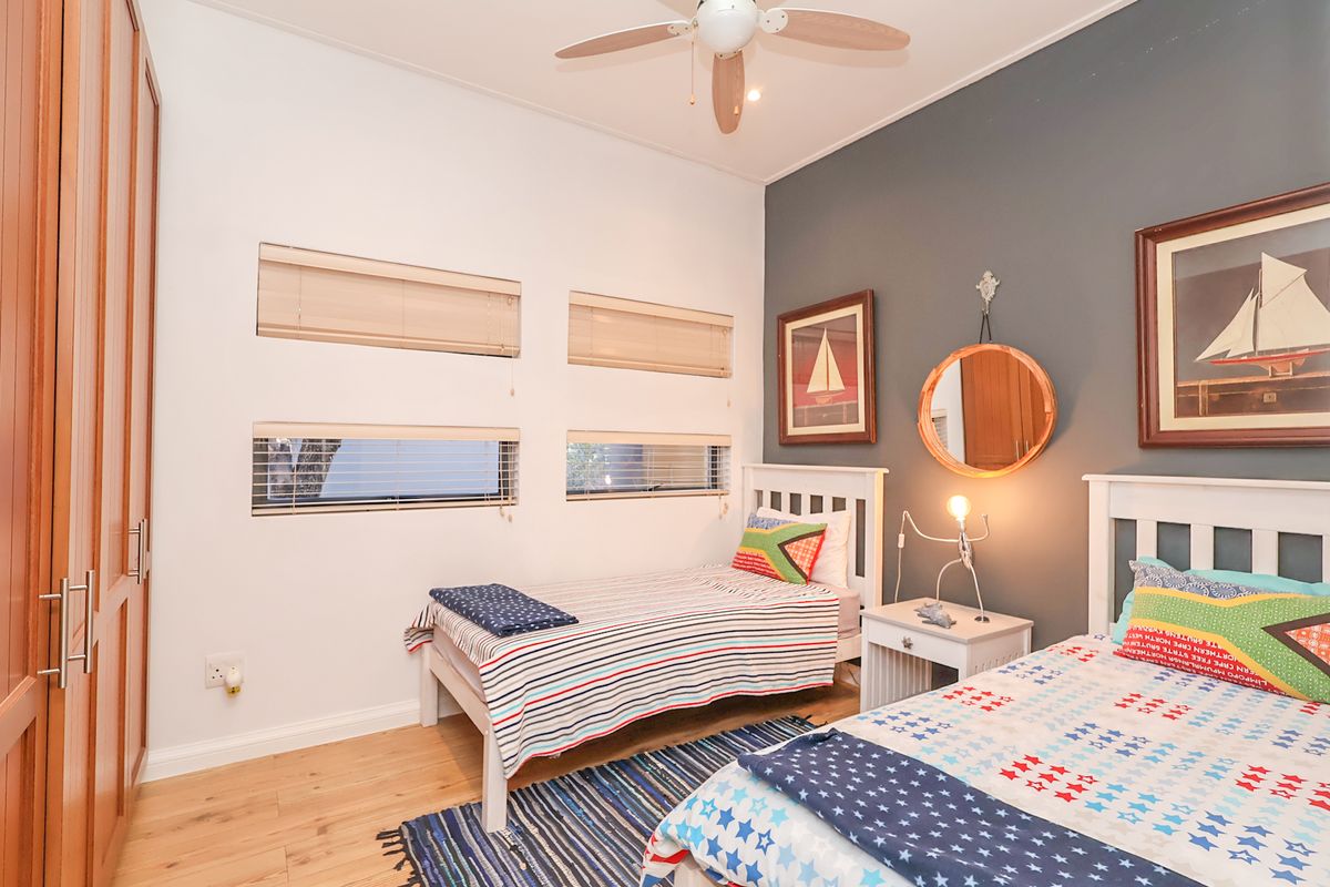 A well-maintained bedroom featuring built-in wooden cupboards, a ceiling fan, and modern horizontal blinds, finished with a neutral and accent wall color scheme.