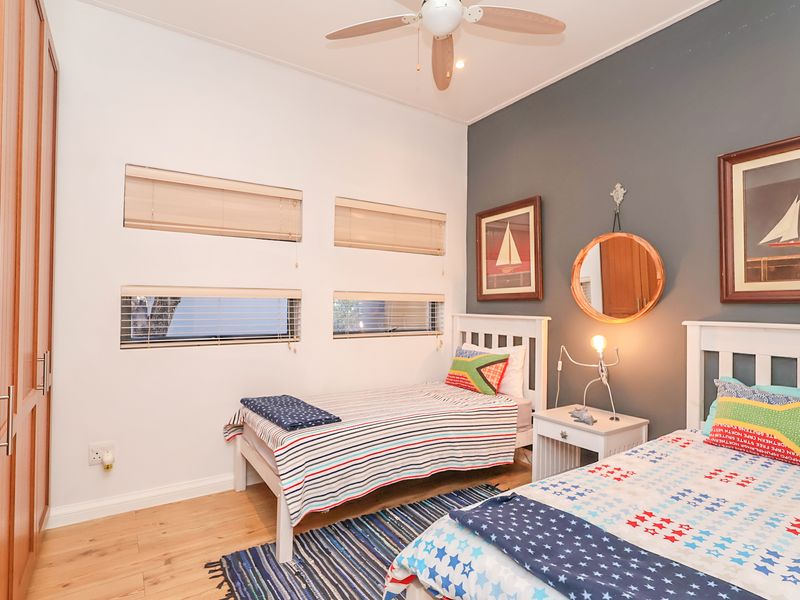 A well-maintained bedroom featuring built-in wooden cupboards, a ceiling fan, and modern horizontal blinds, finished with a neutral and accent wall color scheme.