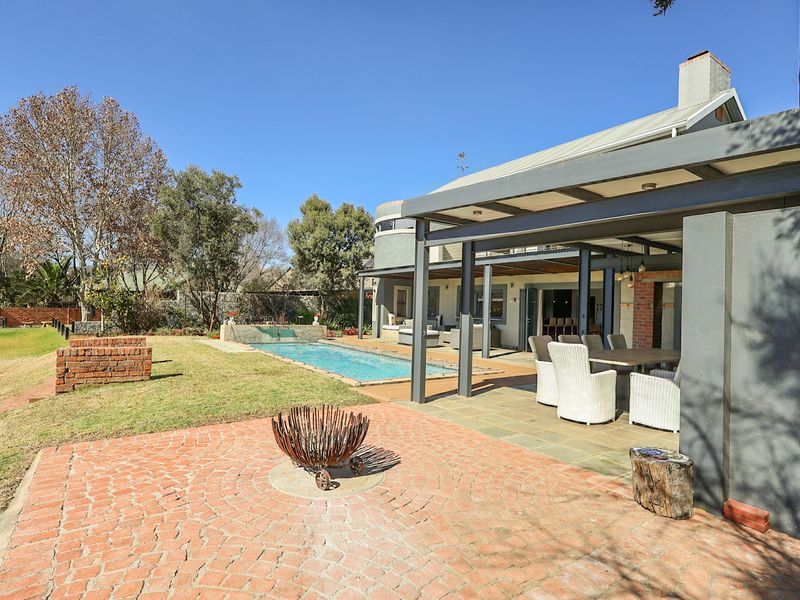 Spacious rear exterior featuring a covered patio, swimming pool with water feature, and a brick-paved outdoor entertainment area set in a landscaped garden.