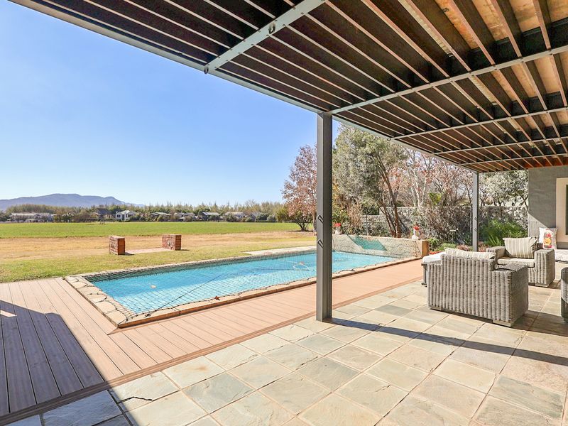 Covered patio area featuring stone paving and timber decking, overlooking a swimming pool with scenic landscape views.