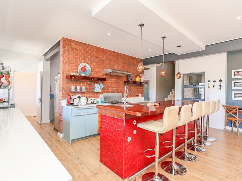 Modern kitchen featuring an exposed brick wall, a large island with a wooden countertop and mosaic tile detail, and contemporary pendant lighting.