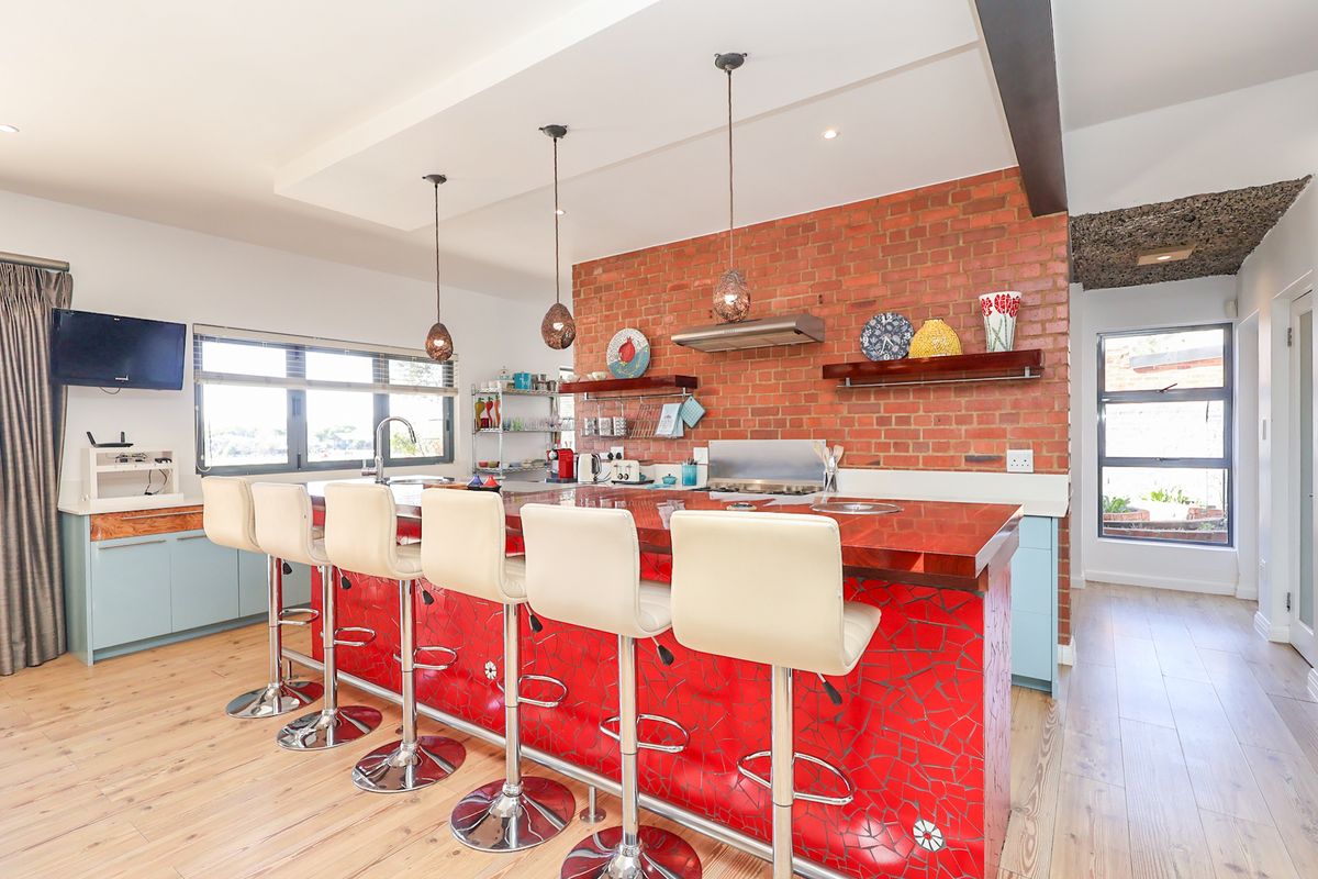 A vibrant kitchen featuring an exposed brick wall, a large island with a mosaic tile base, and modern pendant lighting over the breakfast bar.